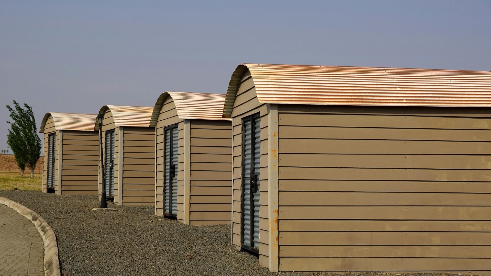 Row of tan beach huts with arched roofs on gravel ground