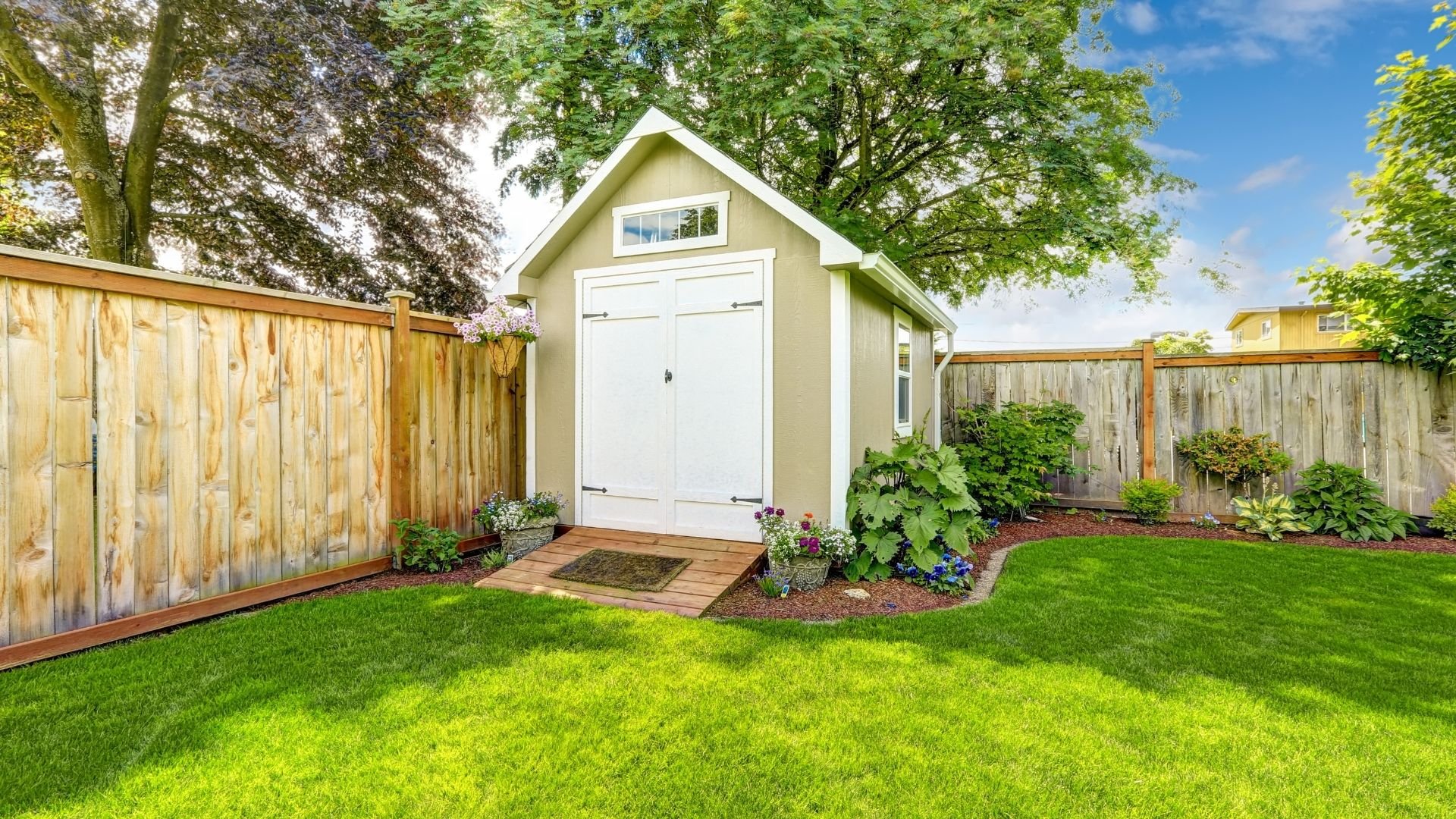 Modern garden shed with white garage door, wooden fencing, and lush green lawn surroundings