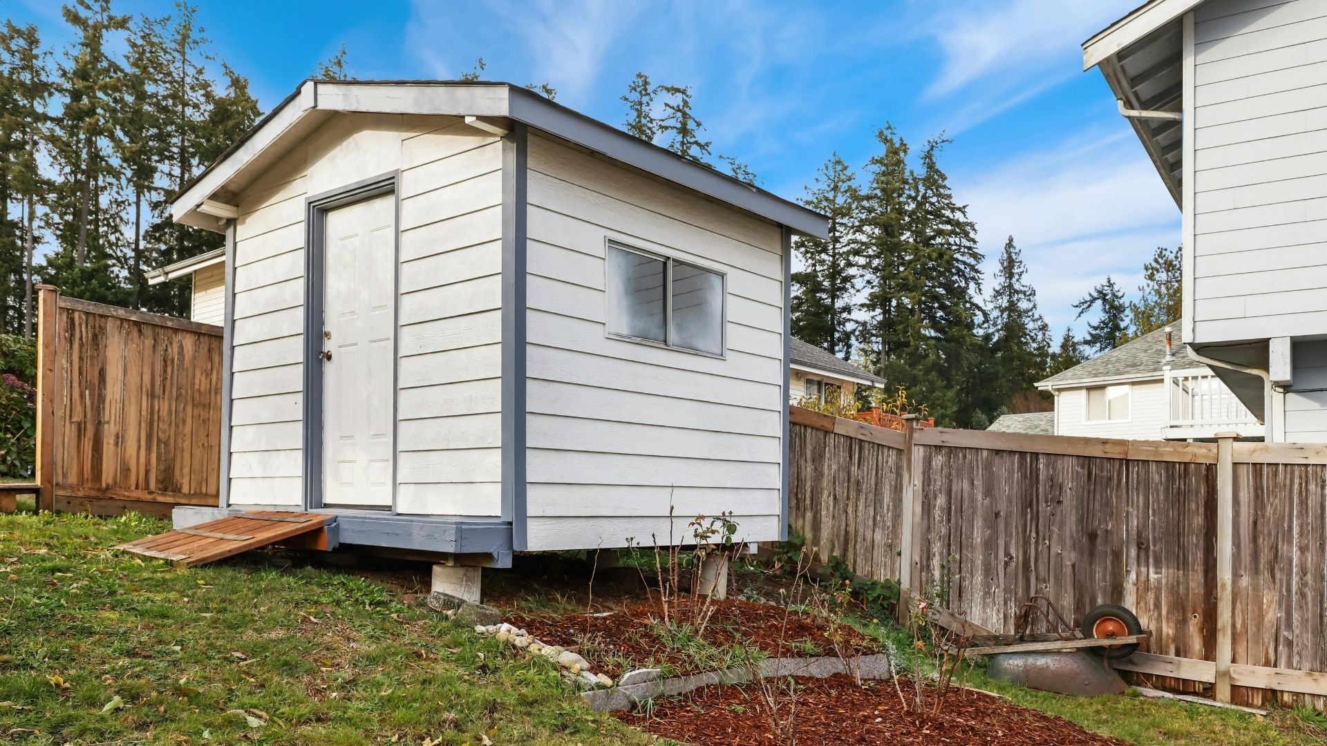 Modern tiny house with white siding surrounded by wooden fences and evergreen trees