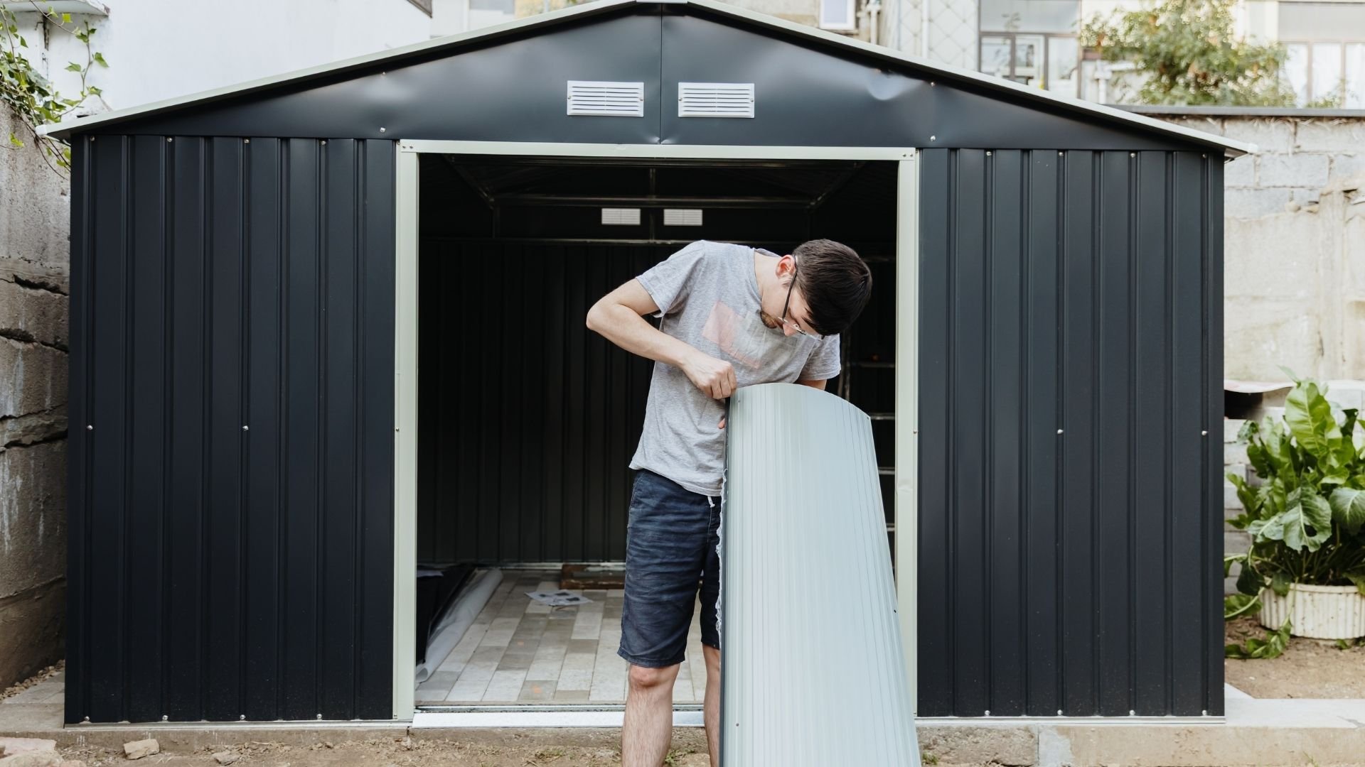 Man installing door on modern black metal garden shed in backyard