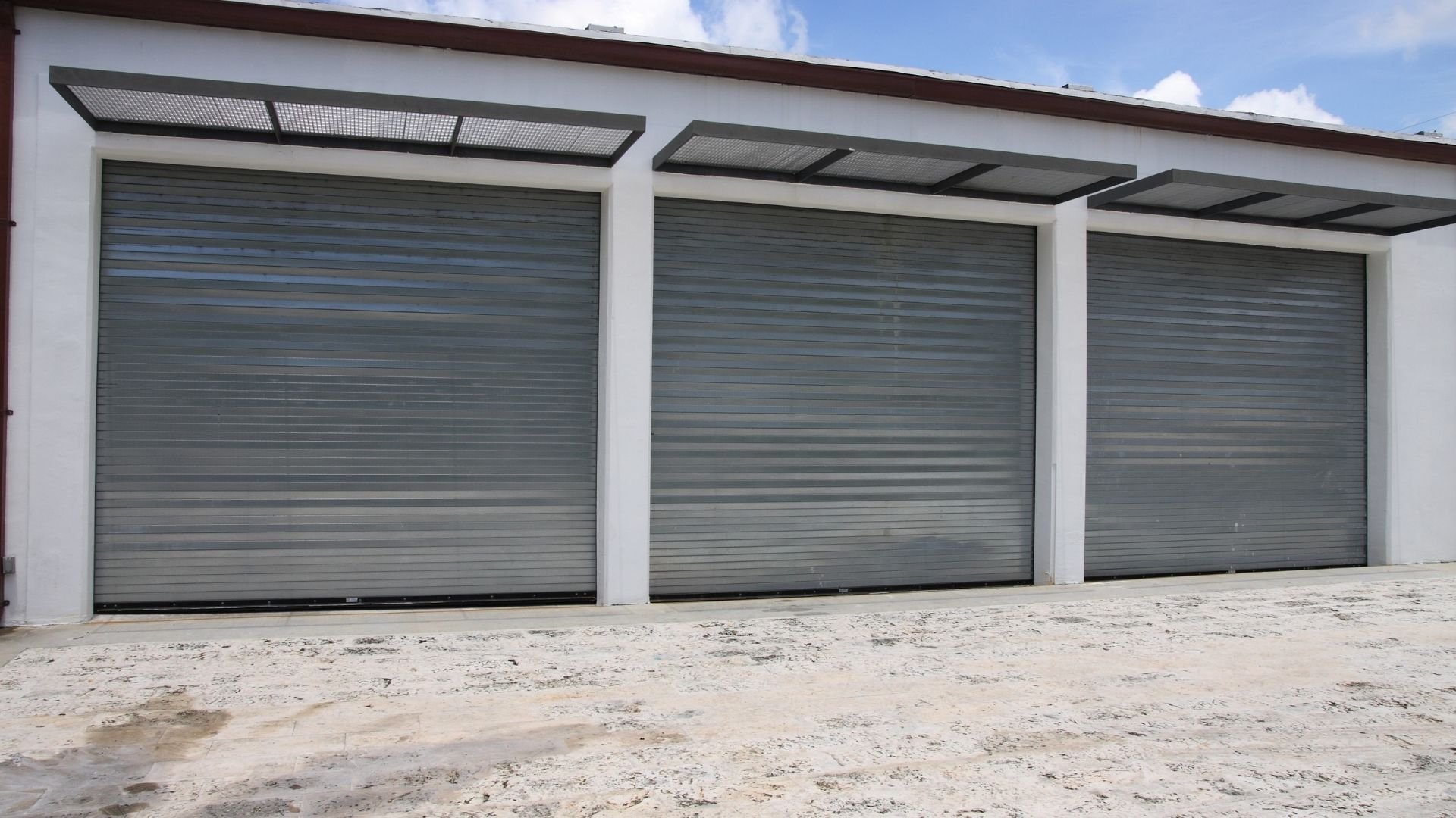 Modern garage with three gray roller doors and white walls under blue sky