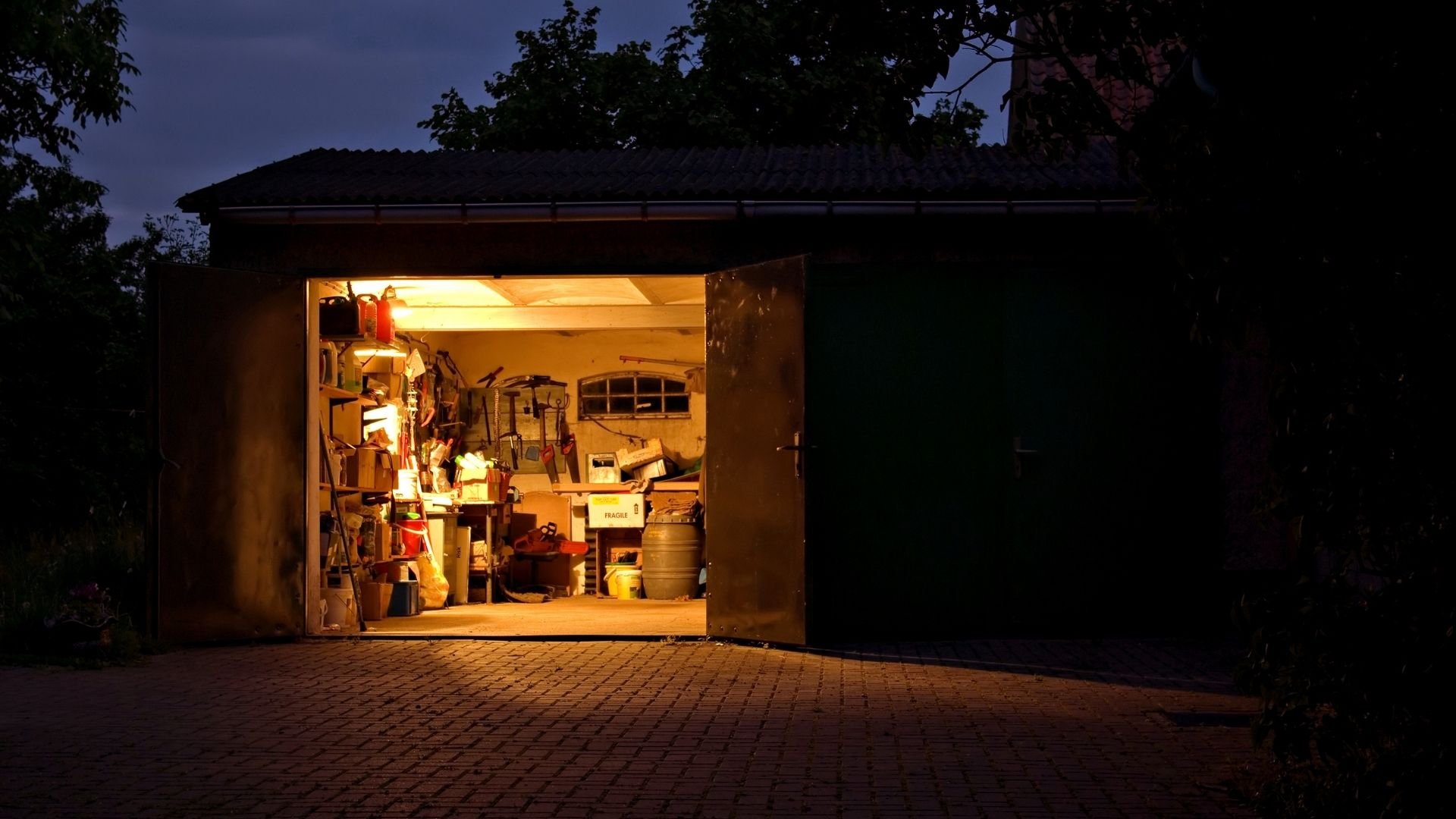 Well-lit garage workshop at dusk filled with tools, equipment, and storage items.
