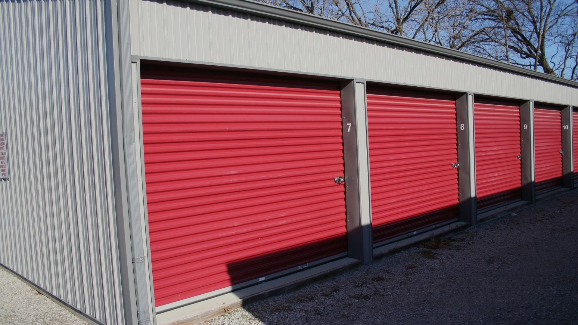 Row of numbered red roll-up storage unit doors on metal building exterior
