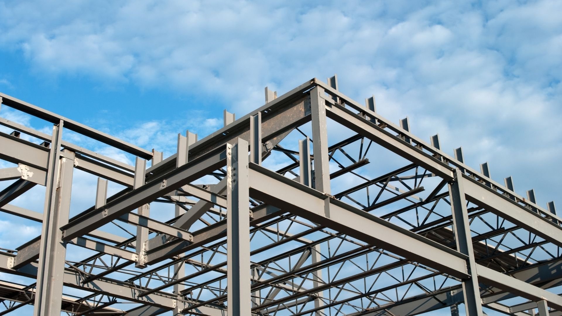 Steel industrial building framework against clear blue sky with white clouds.