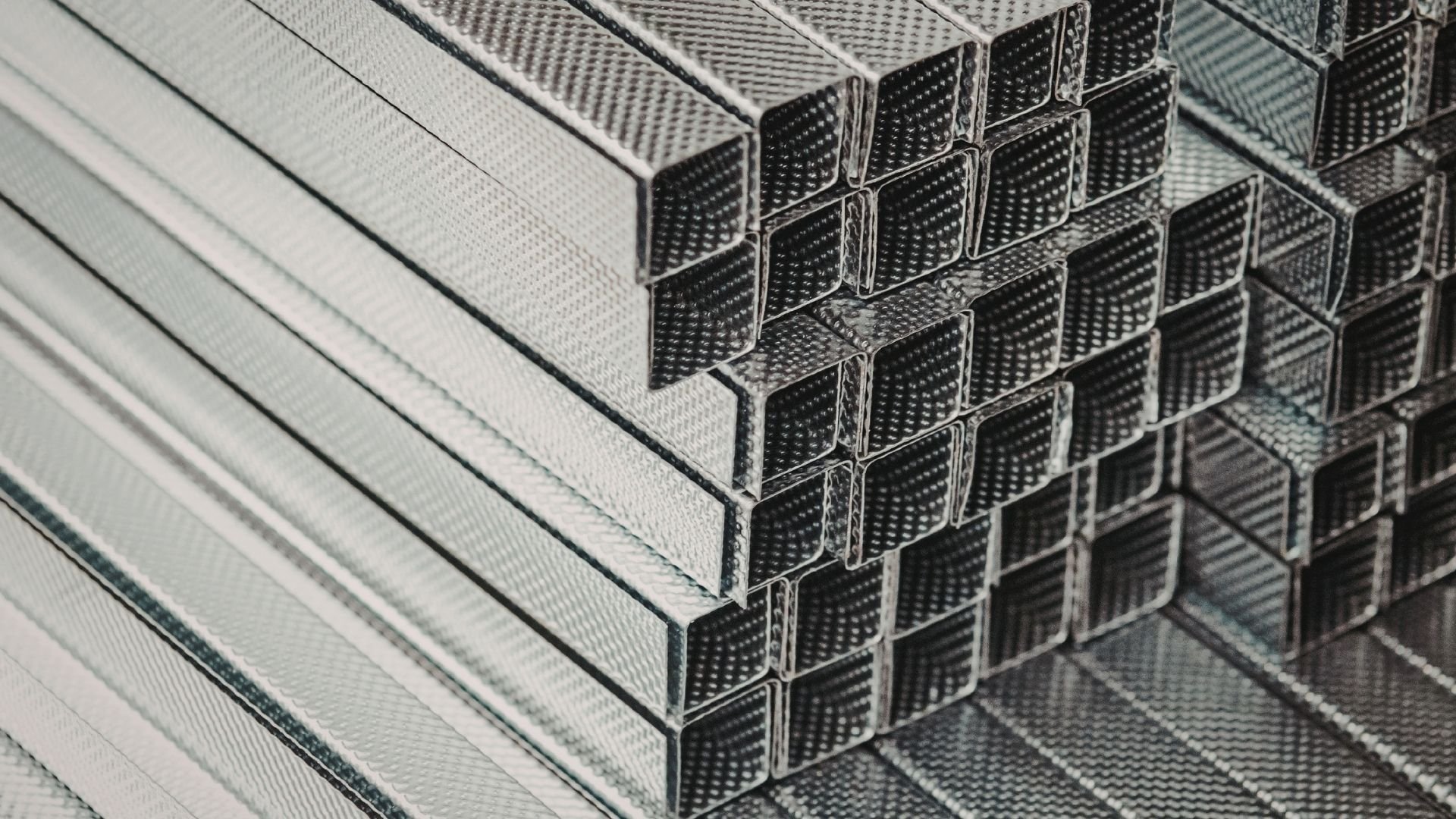 Close-up of stacked metal rectangular tubes with perforated textured surfaces and seams.