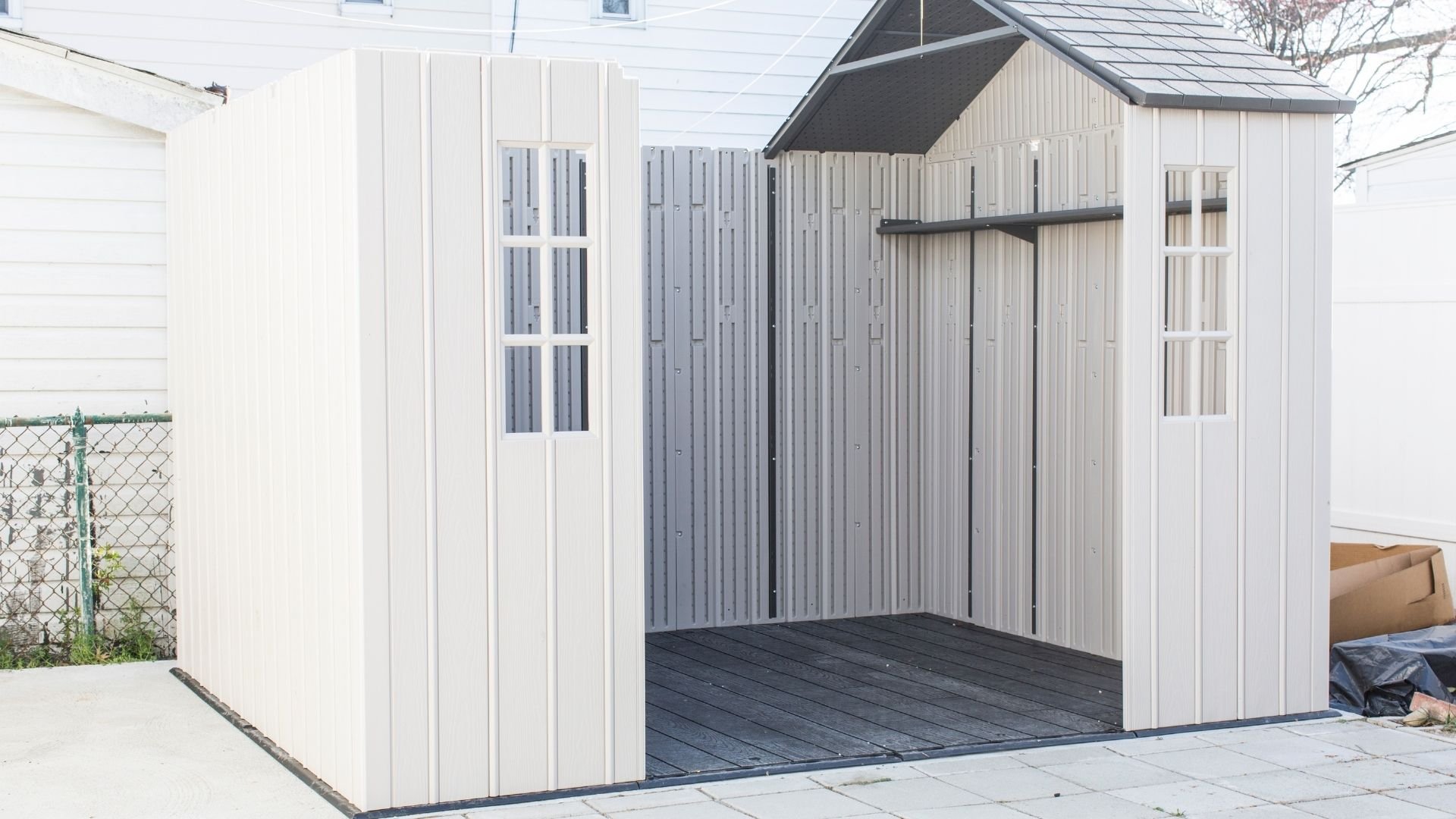 Modern white metal shed with dark gable roof and black wooden deck flooring.