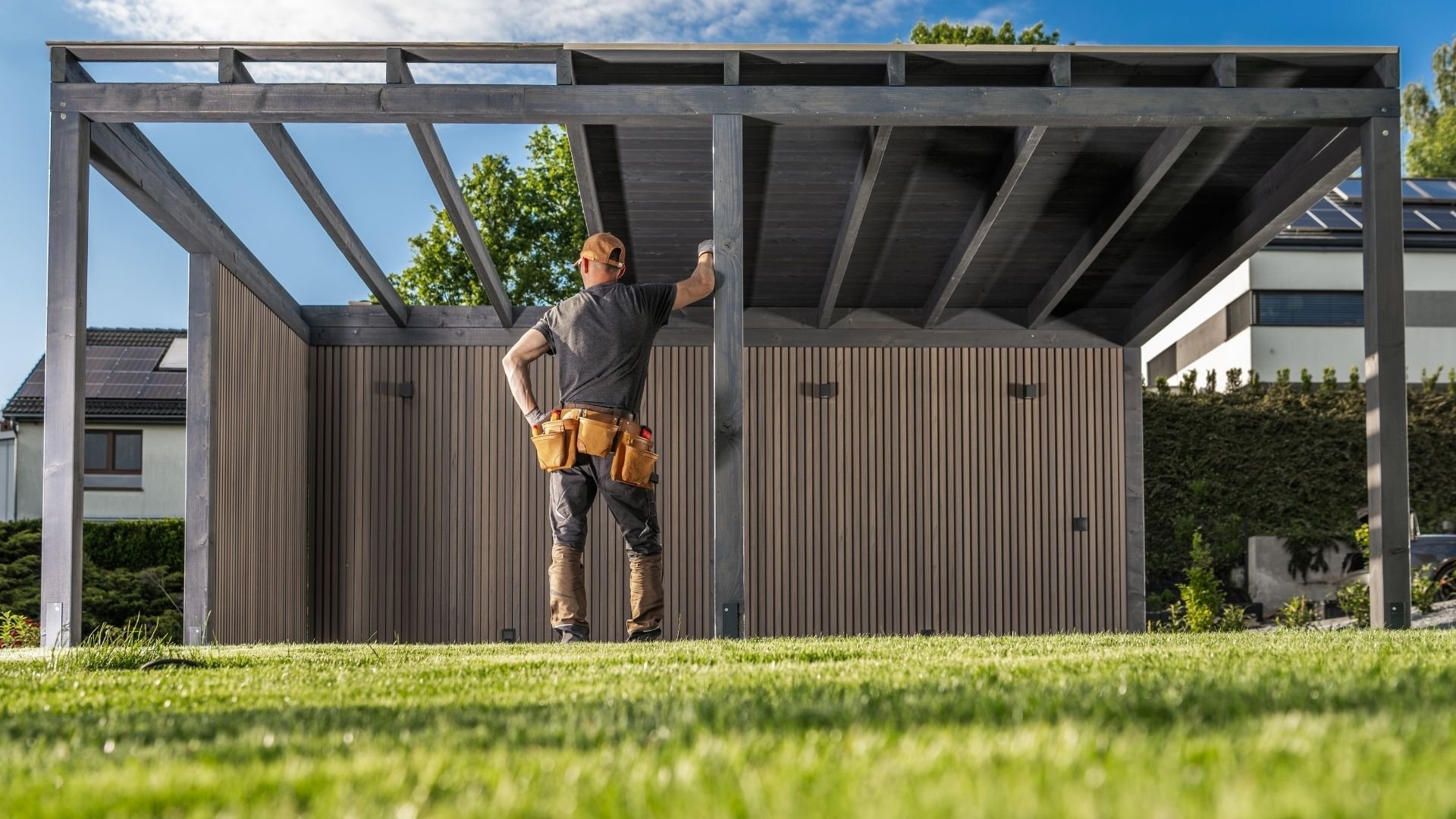 Construction worker with tool belt standing on pergola structure in backyard