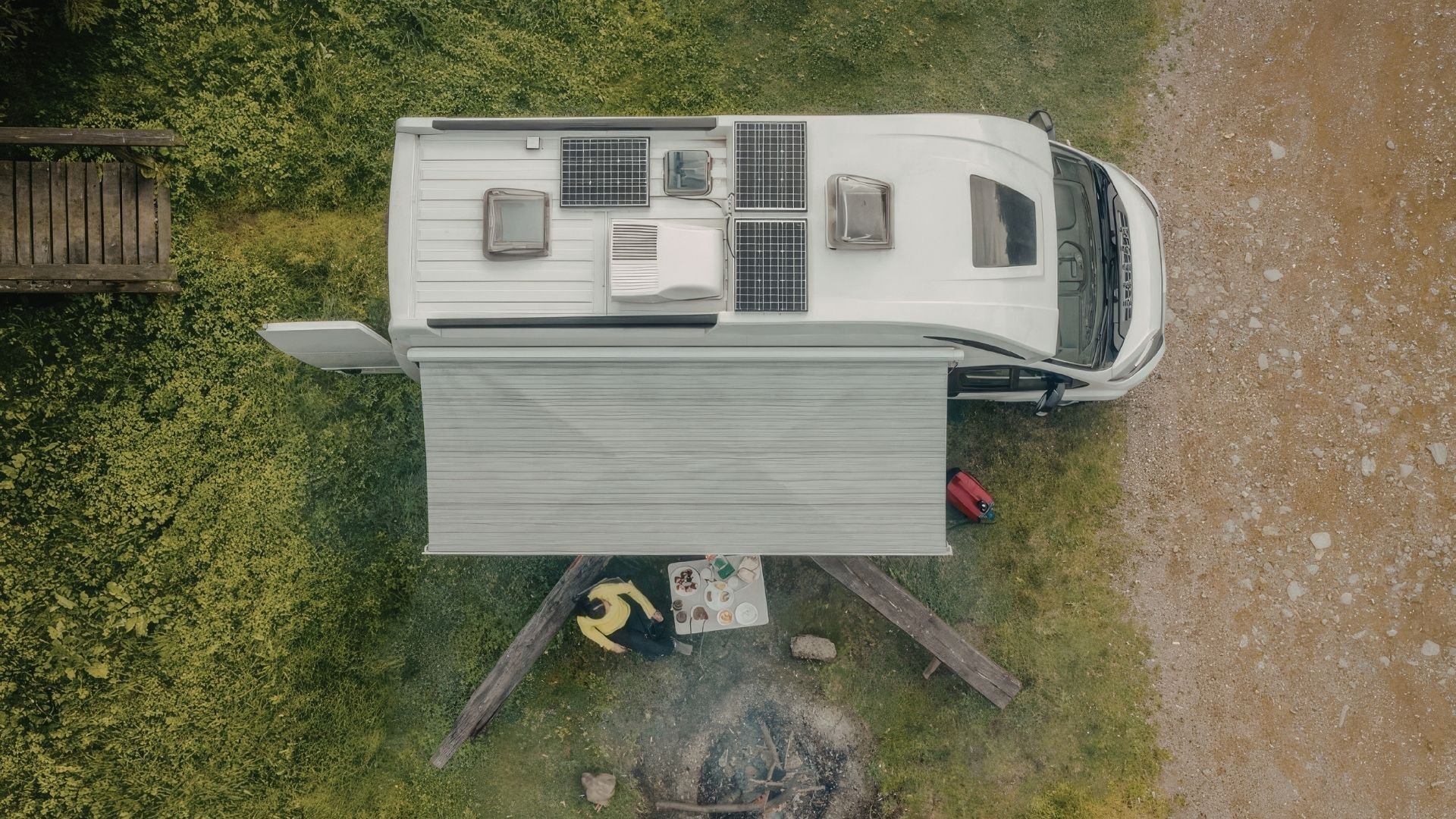 Aerial view of white RV with solar panels parked in nature with awning extended.