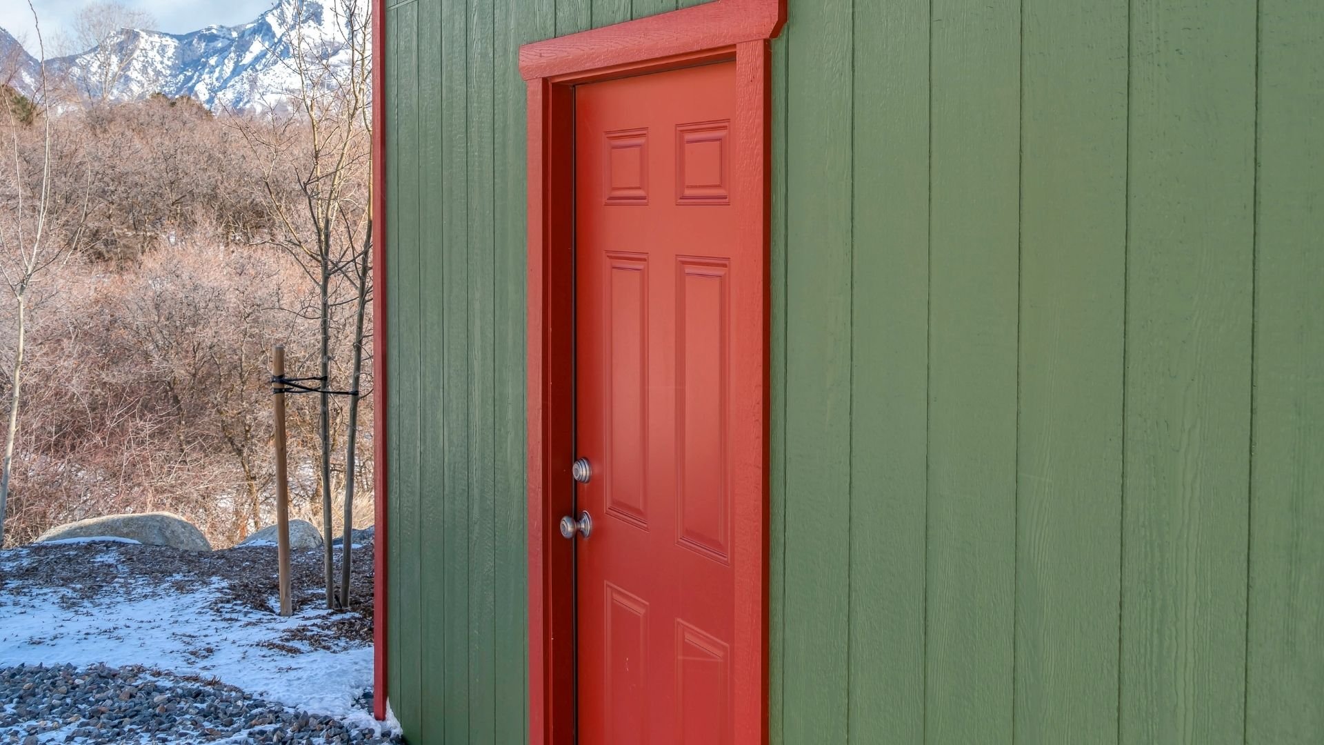 Red door on green building with snowy mountains visible in background