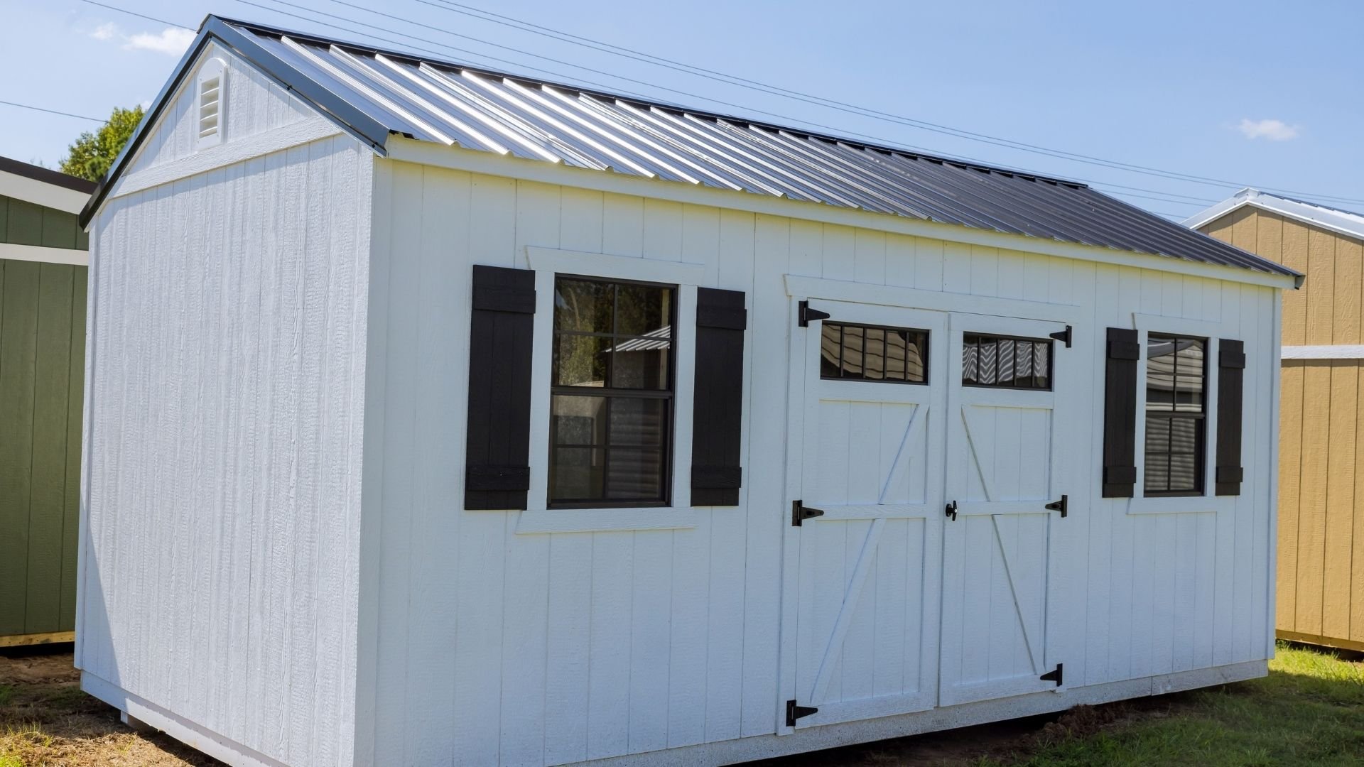 Light blue storage shed with black shutters, windows, and metal roof