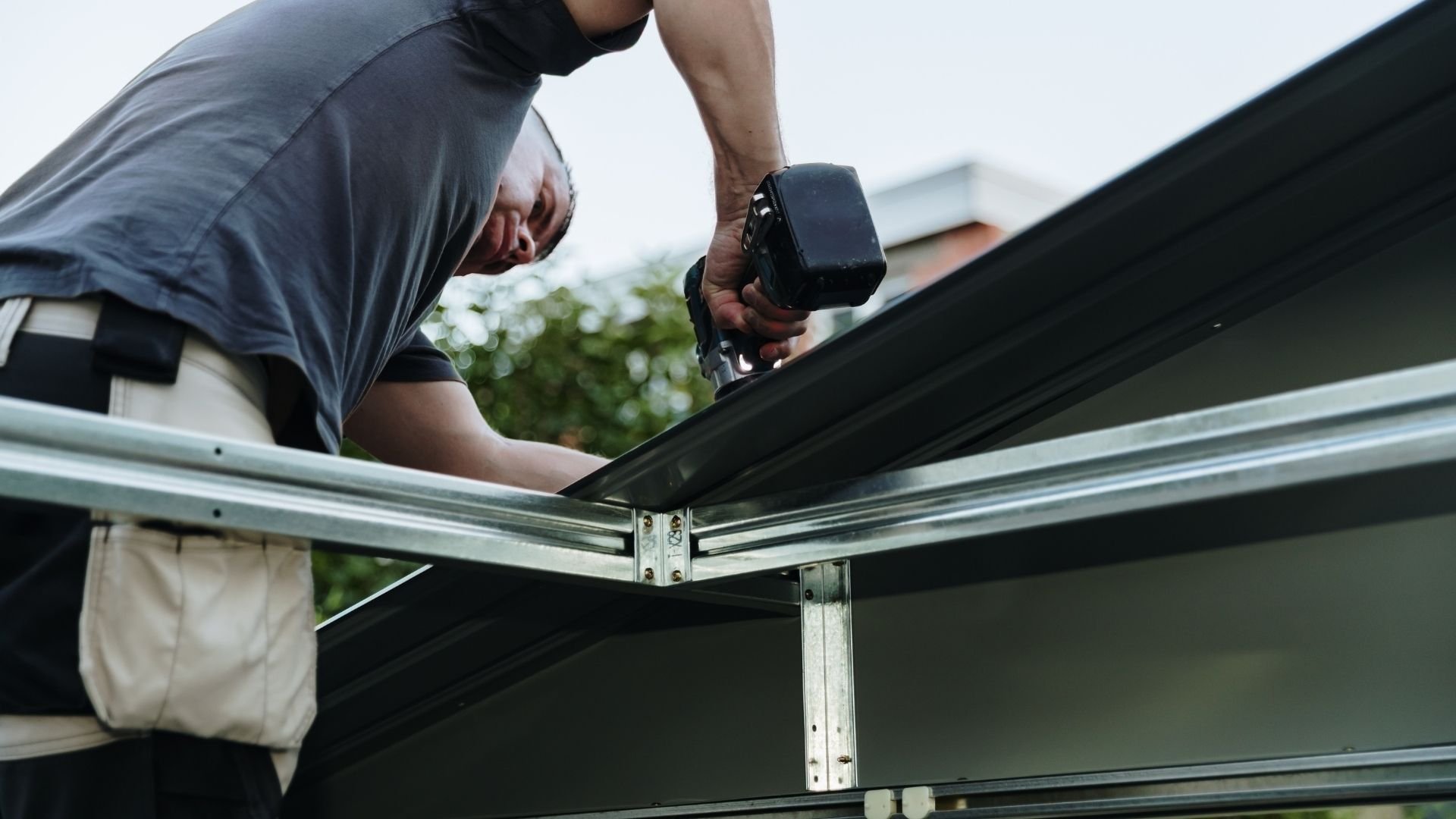 Man using power drill to assemble metal frame outdoors on sunny day
