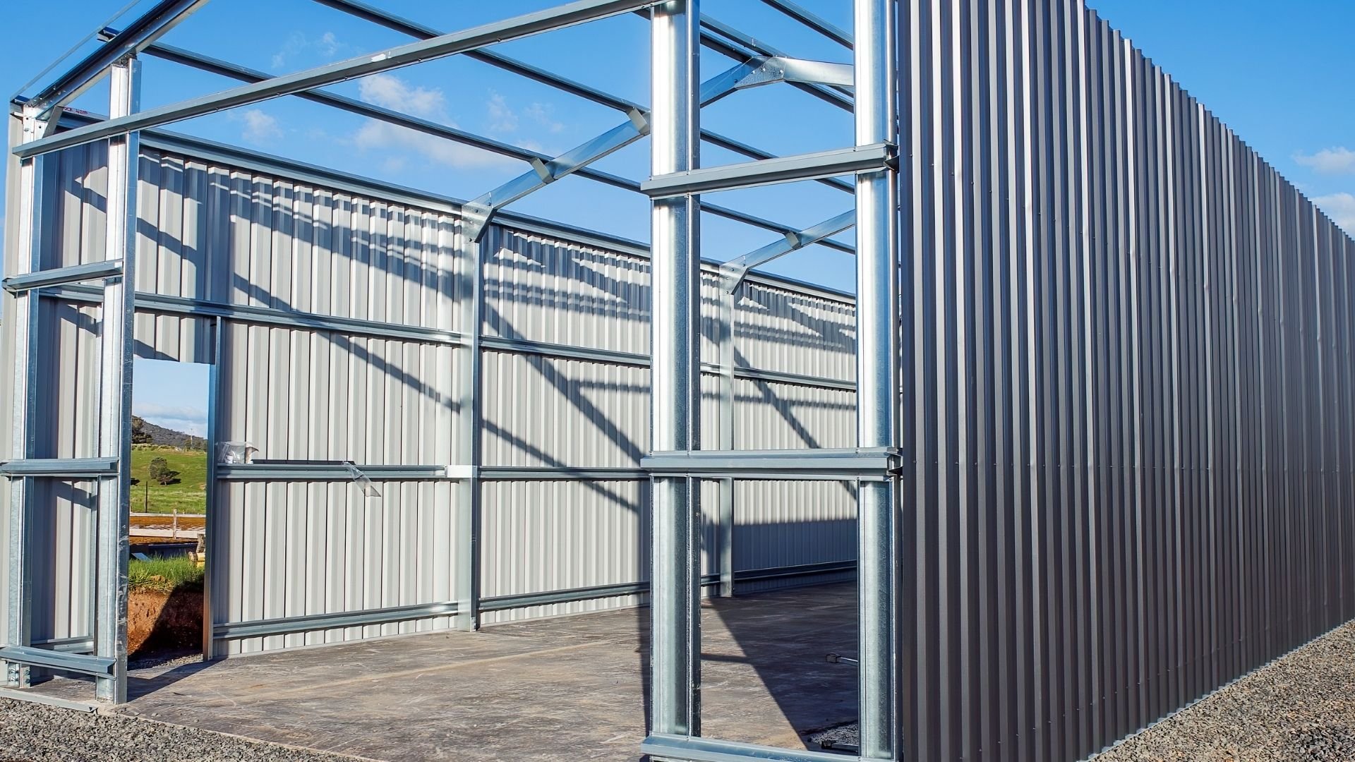 Modern metal greenhouse with corrugated walls and frame structure against blue sky